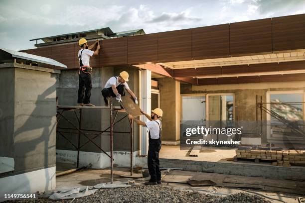 équipe de travailleurs de la construction coopérant tout en travaillant sur une maison extérieure. - artisan batiment photos et images de collection