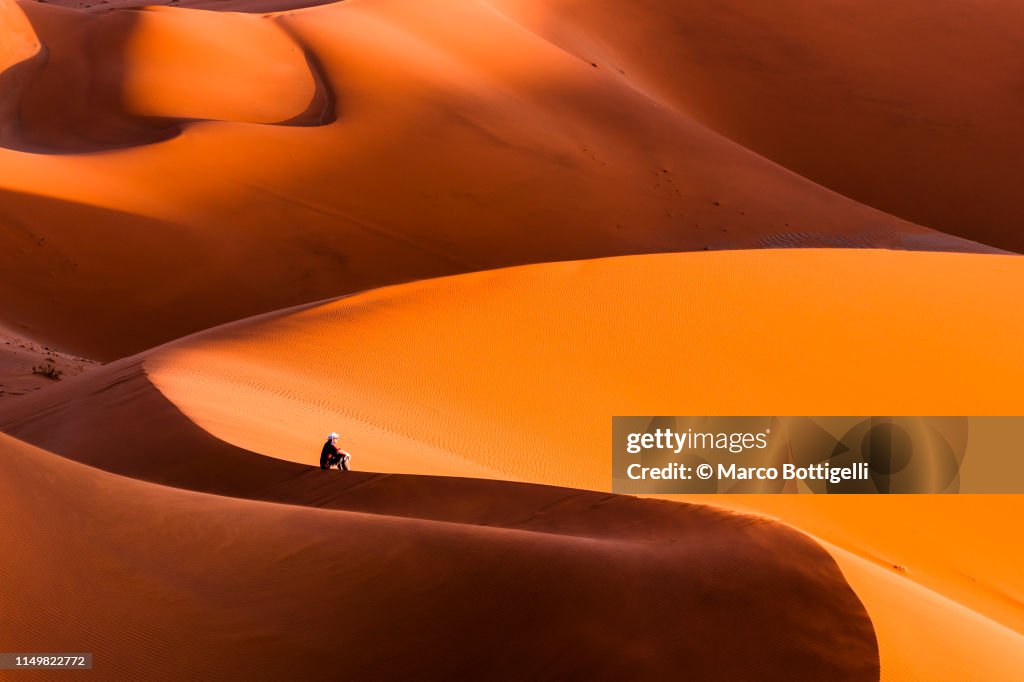Man sitting on top of a giant dune contemplating the sunset, Namibia