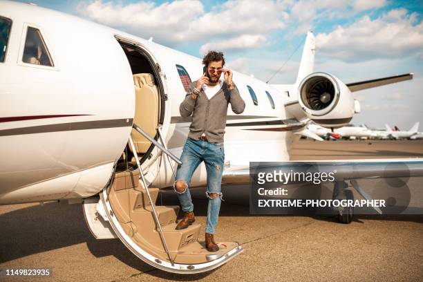young rich man disembarking from a private jet, having a conversation on a smart phone - billionaire stock pictures, royalty-free photos & images