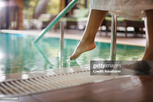 woman in bathrobe dipping toes into swimming pool - spa stock pictures, royalty-free photos & images