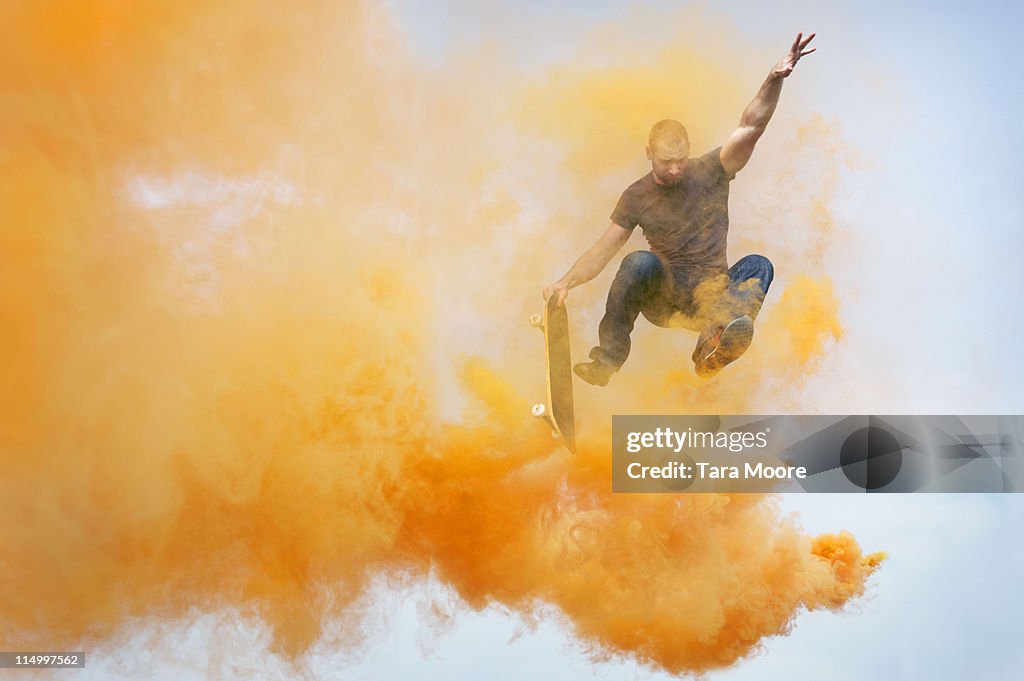 Man jumping through orange smoke with skateboard