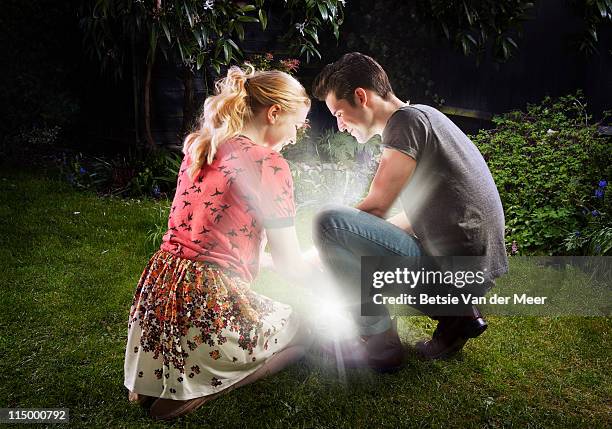 couple crouched, looking at shining light. - finding treasure stock pictures, royalty-free photos & images