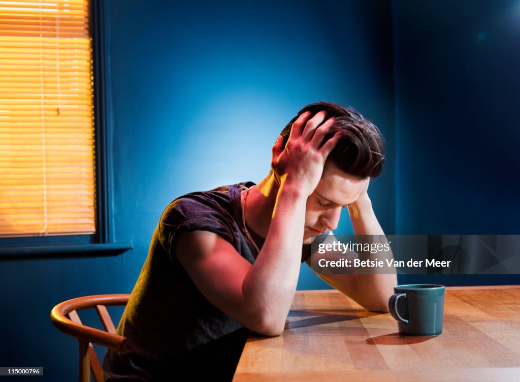 Man sitting with head in hands at table.