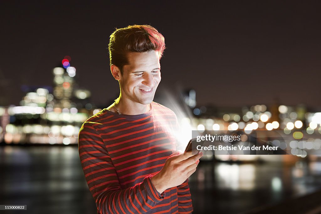 Man laughing,looking at phone in city.