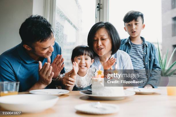 famiglia festeggia insieme il compleanno della bambina - parents children blow candles asians foto e immagini stock