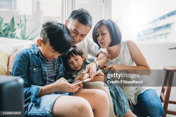 familie met behulp van een mobiele telefoon samen zittend op de bank thuis - taiwanese ethnicity stockfoto's en -beelden