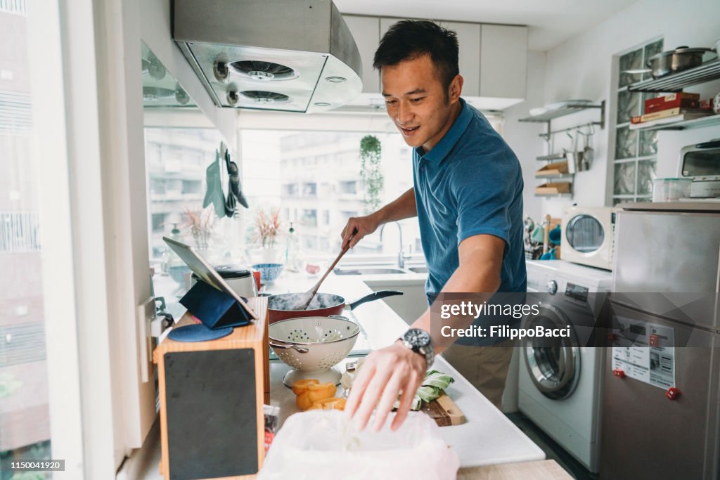 Hombre preparando la cena en la cocina viendo una receta en la tableta