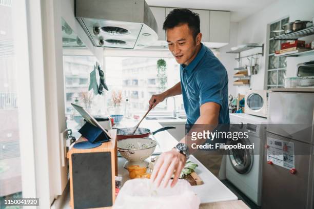 man preparing dinner in the kitchen watching a recipe on the tablet - taiwanese stock pictures, royalty-free photos & images