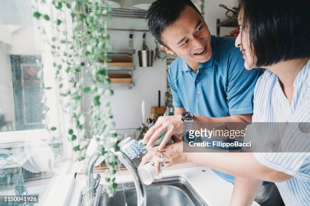 adult couple washing dishes together in the kitchen at home - shower man woman washing stock pictures, royalty-free photos & images