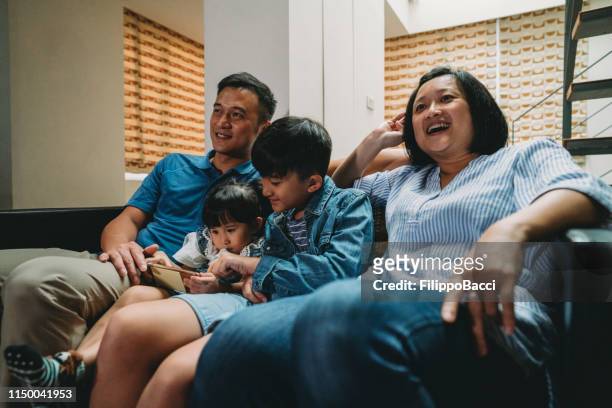 familie schaut zu hause gemeinsam auf dem sofa fern - taiwanese ethnicity stock-fotos und bilder