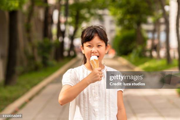 ein kleines mädchen isst eis aus einem kegel in einem öffentlichen park - girl eating messy ice cream cone stock-fotos und bilder