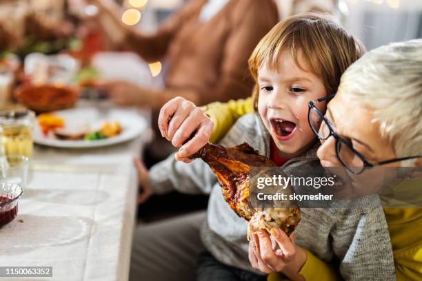 playful grandmother and grandson biting turkey leg during lunch at home. - turkey leg stock pictures, royalty-free photos & images