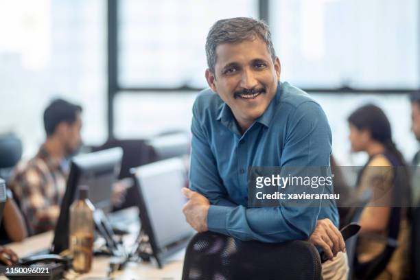 manager maturo sorridente seduto in ufficio creativo - india foto e immagini stock
