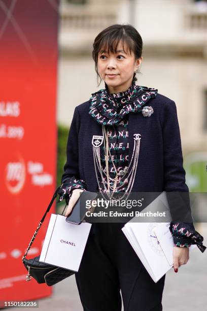Guest wears a Chanel ruffled blouse, a Chanel tweed camellia brooch, a black tweed jacket, a black Chanel belt-bag, black pants , outside the Chanel...