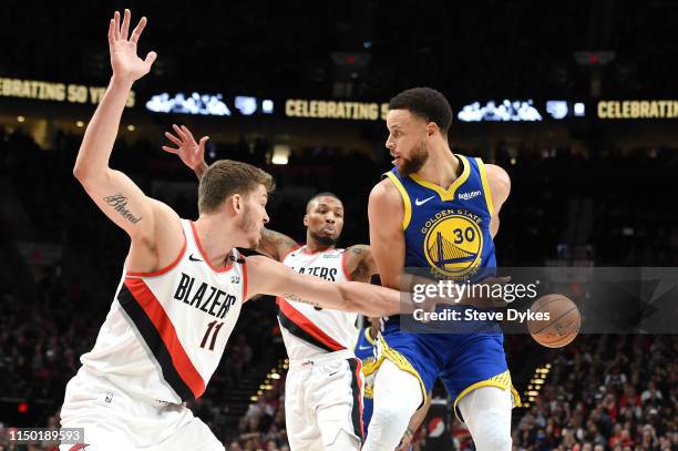 Stephen Curry of the Golden State Warriors passes the ball behind his back against Meyers Leonard and Damian Lillard of the Portland Trail Blazers...