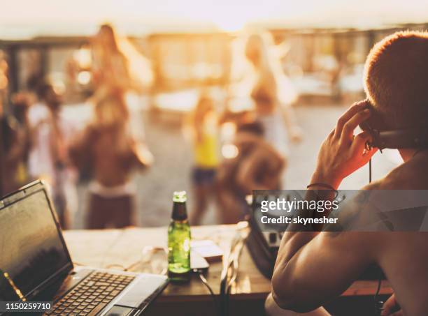 back view of a dj with headphones on a beach party at sunset. - dj summer stock pictures, royalty-free photos & images