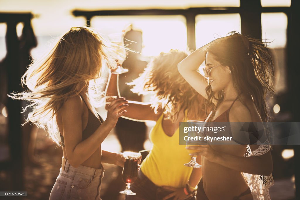 Young beautiful women dancing on the beach party at sunset.