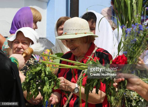 Faithful put green branches and grasses under holy water, which is sprinkled by the priest on parishioners in Kyiv, Ukraine, June 16, 2019. Eastern...