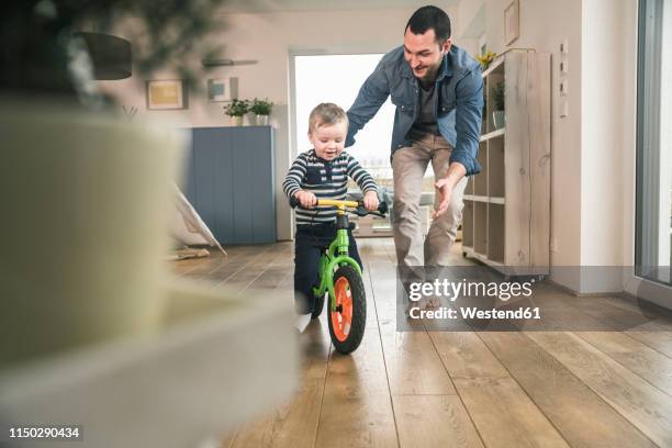 father helping son riding with a balance bicycle at home - child and parent and bike stock-fotos und bilder