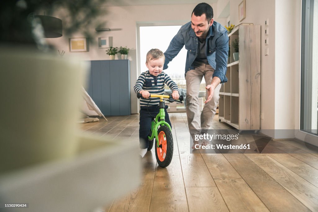 Father helping son riding with a balance bicycle at home