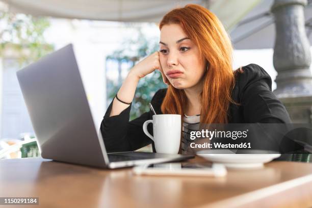 portrait of redheaded young woman at pavement cafe looking at laptop - hands on face stock-fotos und bilder