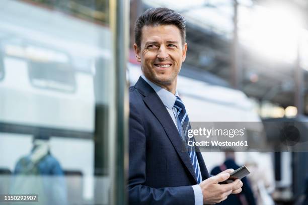 smiling businessman with cell phone at train station - costume suisse photos et images de collection