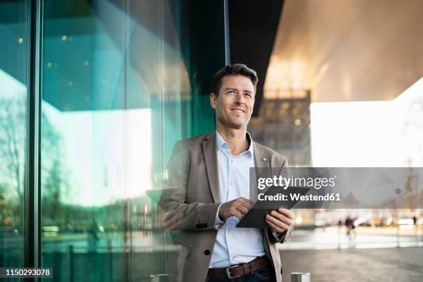 smiling businessman using tablet outside a building in the city - schweiz business stock-fotos und bilder