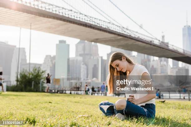 young woman exploring new york city, taking a break, reading book - brooklyn bridge park stock-fotos und bilder