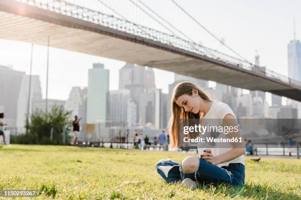 young woman exploring new york city, taking a break, reading book - brooklyn bridge park foto e immagini stock