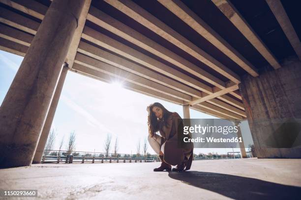 young woman crouching at an underpass in backlight - underpass stock pictures, royalty-free photos & images