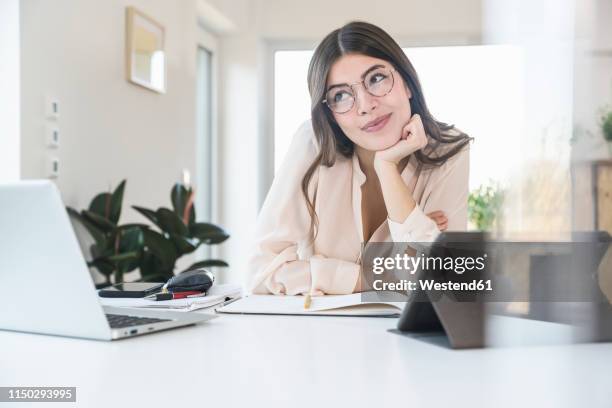 portrait of smiling young woman sitting at table at home - student day dreaming stock pictures, royalty-free photos & images