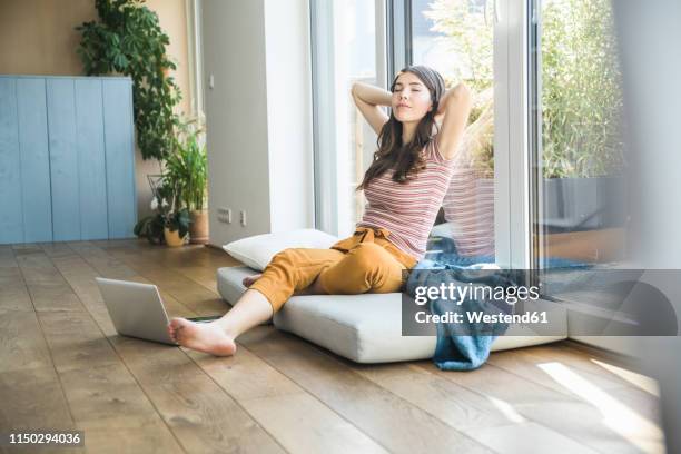 relaxed young woman sitting at the window at home with laptop - digital detox stock pictures, royalty-free photos & images