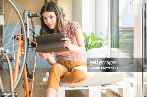 young woman with tablet reparing bicycle at home - tutorial stock-fotos und bilder