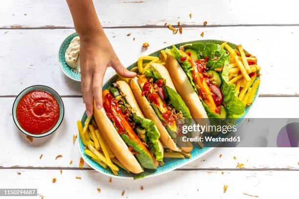 hot dogs with french fries, ketchup and mayonnaise, hand taking an hot dog - hand white background stock pictures, royalty-free photos & images