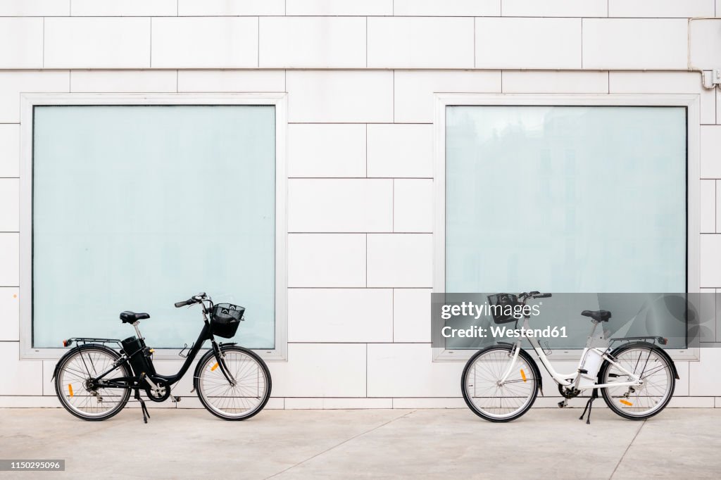 Two e-bikes at a white wall with two windows