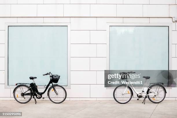 two e-bikes at a white wall with two windows - sustainable transportation stock pictures, royalty-free photos & images