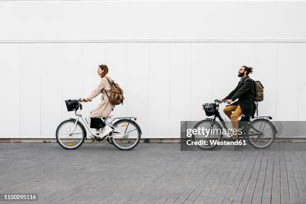 couple riding e-bikes along a white wall in the city - ebike stock pictures, royalty-free photos & images