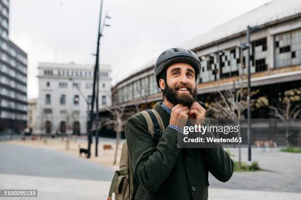 portrait of smiling man putting on bicycle helmet in the city - sustainable transportation stock pictures, royalty-free photos & images