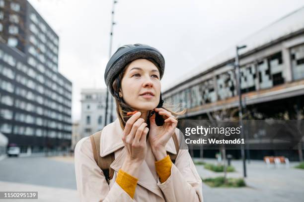 portrait of woman putting on bicycle helmet in the city - cycling helmet stock-fotos und bilder
