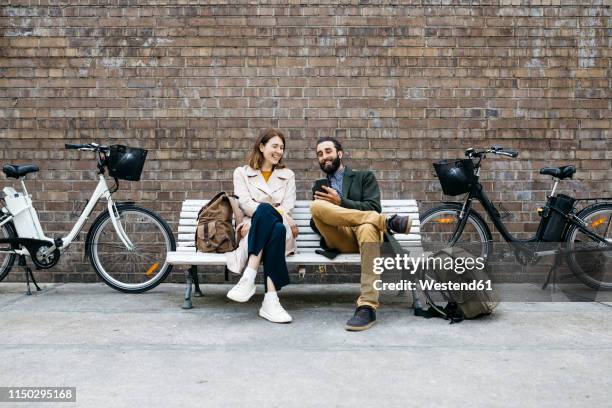 happy couple sitting on a bench next to e-bikes sharing cell phone - wall e stock pictures, royalty-free photos & images