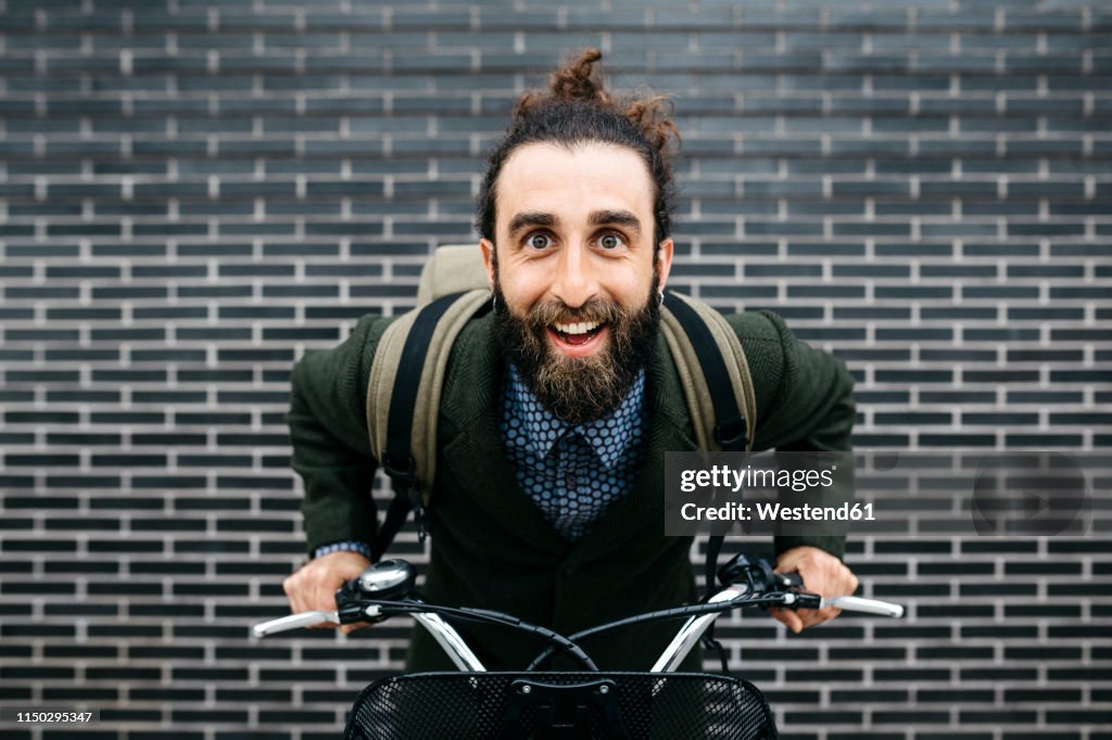 Portrait of happy man with e-bike at a brick wall