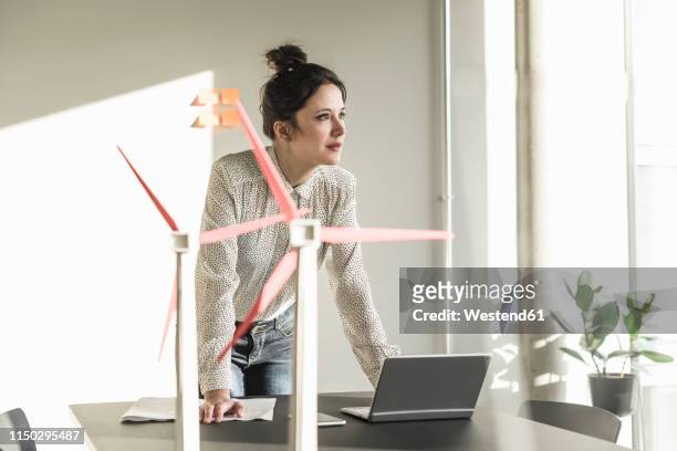 businesswoman with wind turbine models and laptop on desk in office - smarter working stock-fotos und bilder