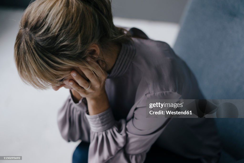 Sad woman sitting in armchair with head in hands