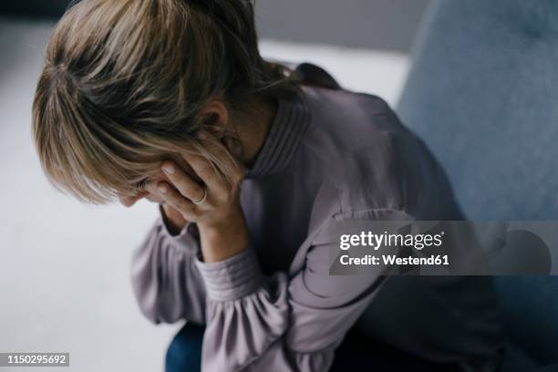 sad woman sitting in armchair with head in hands - hålla huvudet i händerna bildbanksfoton och bilder