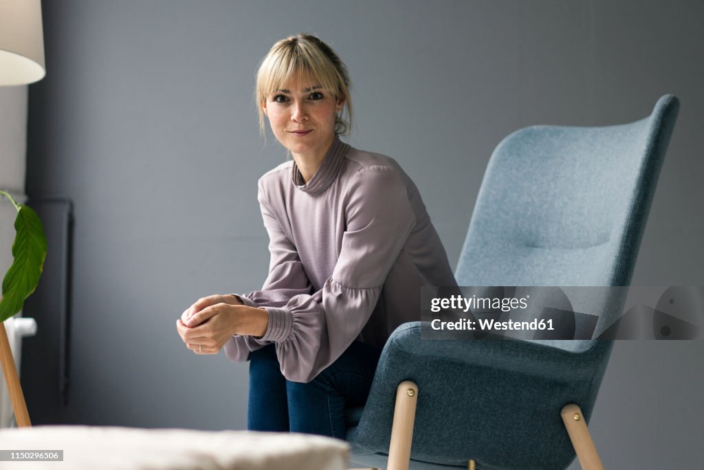 Blond woman sitting in armchair, looking at camera