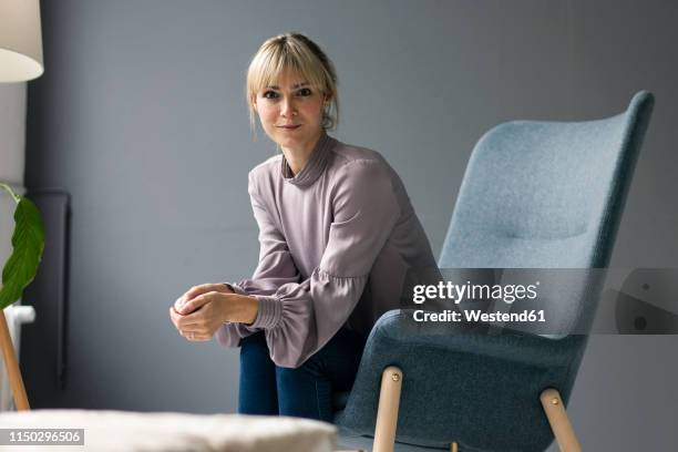 blond woman sitting in armchair, looking at camera - donna poltrona foto e immagini stock