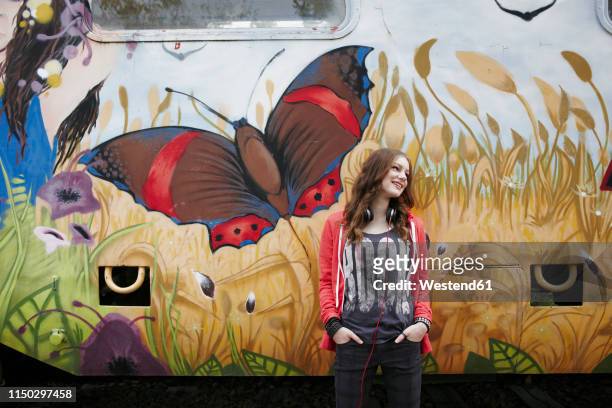 smiling teenage girl standing at a painted train car - hoodie headphones - fotografias e filmes do acervo