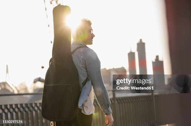 young man with guitar case in the city at sunset - guitar case fotografías e imágenes de stock