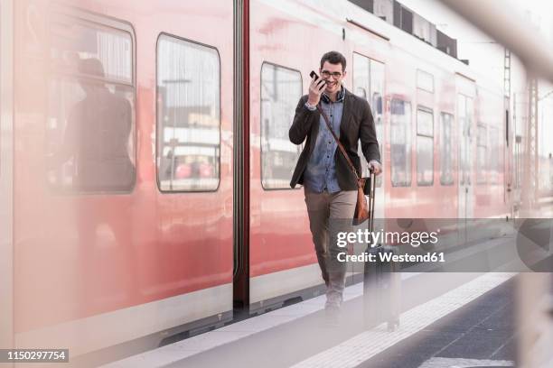 happy young man with cell phone walking on station platform along commuter train - railroad station platform stockfoto's en -beelden