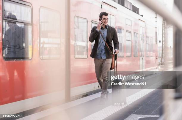 smiling young man on cell phone walking on station platform along commuter train - pendler zug stock-fotos und bilder